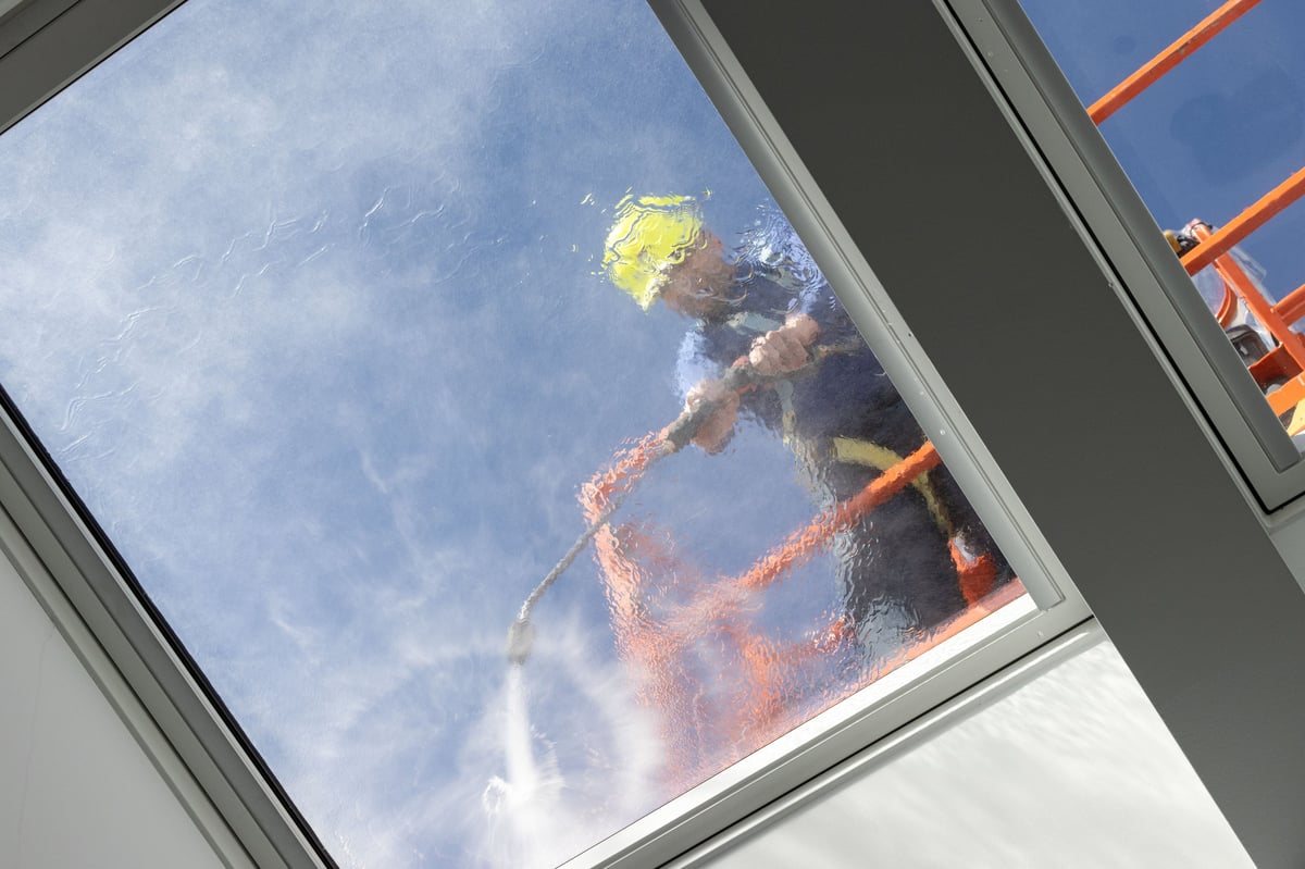 A worker on a cherry picker cleaning roof windows with a high pressure water jet